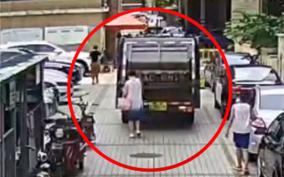 惊险！女子走路看手机 被卷入垃圾车底